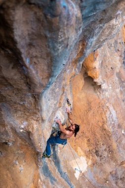 Güçlü bir kaya tırmanıcısı sarkık bir kayaya tırmanıyor. Uzun saçlı genç bir sporcu kayaya tırmanıyor..