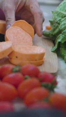 Dikey çekim. Vejetaryen yemeği hazırlıyorum. Bir adam soyulmuş tatlı patatesi tahta bir kesme tahtasıyla dilimliyor. Sağlıklı beslenme. Kapat