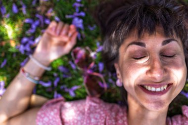 Yaz havası. Yeşil çimlerin ve çiçeklerin üzerinde yatan genç bir kadın. Yaz havası. Kız dışarıda vakit geçiriyor. Doğanın ve tatilin tadını çıkar. Mutlu kadın..