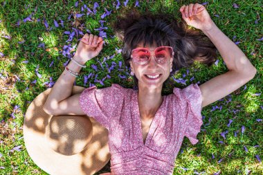 Yeşil çimlerin üzerinde yatan genç bir kadın. Yaz havası. Kız dışarıda vakit geçiriyor. Doğanın tadını çıkar. Üst Manzara. Sağlıklı gülümseyen kız baharda çimlerde.