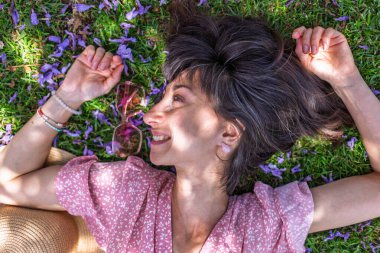 Yaz havası. Yeşil çimlerin ve çiçeklerin üzerinde yatan genç bir kadın. Yaz havası. Kız dışarıda vakit geçiriyor. Doğanın ve tatilin tadını çıkar. Mutlu kadın..