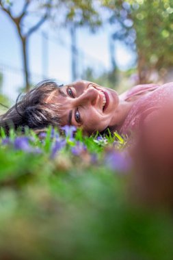 Yeşil çimlerin üzerinde yatan genç bir kadın. Yaz havası. Kız dışarıda vakit geçiriyor. Doğanın tadını çıkar. Sağlıklı gülümseyen kız baharda çimlerde.