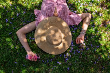 Hasır şapkalı mutlu kız yaz parkında yeşil çimlerin üzerinde uzanmış, manzaralı. Yaz havası. Kız dışarıda vakit geçiriyor. Doğanın tadını çıkar.