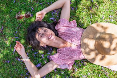 Yaz havası. Yeşil çimlerin ve çiçeklerin üzerinde yatan genç bir kadın. Yaz havası. Kız dışarıda vakit geçiriyor. Doğanın ve tatilin tadını çıkar. Mutlu kadın..