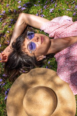 Yeşil çimlerin üzerinde yatan genç bir kadın. Yaz havası. Kız dışarıda vakit geçiriyor. Doğanın tadını çıkar. Sağlıklı gülümseyen kız baharda çimlerde.