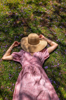 Hasır şapkalı mutlu kız yaz parkında yeşil çimlerin üzerinde uzanmış, manzaralı. Yaz havası. Kız dışarıda vakit geçiriyor. Doğanın tadını çıkar.