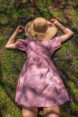 Yeşil çimenlerin ve çiçeklerin üzerinde yatan genç bir kadın. Şapka yüzünü örtüyor. Yaz havası. Kız dışarıda vakit geçiriyor. Doğanın tadını çıkar.