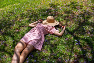 Hasır şapkalı mutlu kız yaz parkında yeşil çimlerin üzerinde uzanmış, manzaralı. Yaz havası. Kız dışarıda vakit geçiriyor. Doğanın tadını çıkar.
