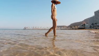 İnce bir kız İsrail 'deki Ölü Deniz plajında geziniyor. Kavramsal seyahat ve rahatlama.