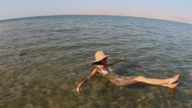 Ölü Deniz 'de dinlenen bir kadın, beyaz bir kumsalın açık ve sığ sularında yüzerek talassoterapi görüyor.