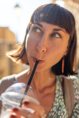 Kokteylli güzel bir esmer. Paket kahve. Güneşli bir yaz gününde pipetle kokteyl içen mutlu genç bir kadının portresi. Soğuk içecek..