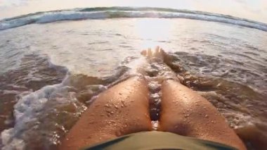 Sahilde bir kız okyanus dalgalarının tadını çıkarıyor. Bakış açısı. Bacaklarını yakın çekim. Mayo giymiş bir kadın temiz bir yerde güneşlenir ve dinlenir.