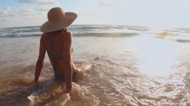 Deniz kenarında okyanus dalgalarının tadını çıkaran bir kız. Mayolu bir kadın temiz kumsalda güneşleniyor ve dinleniyor.