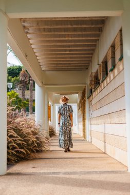 Şapka takan güzel bir bayanın tam boy fotoğrafı. Sokakta yürümek, güneşli hava, hafta sonu. Elbiseli ve şapkalı genç bir kız sokakta yürüyor..