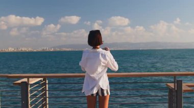 Elinde kamera olan bir kadın blogcu denizin kenarında durup fotoğraf çekiyor. Şık bir kadın fotoğraf makinesiyle fotoğraf çekiyor. Bir kadın.