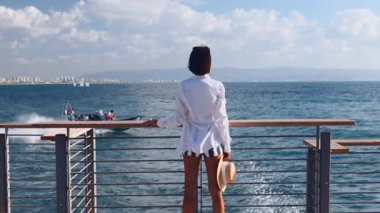 Şapkalı bir kadın bir geminin geçişini izliyor. Kız denizin ve dalgaların güzelliğinin tadını çıkarıyor. Kız rahatlıyor..