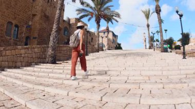 Bir kız seyahat ediyor. Seyahat ve macera. Sırt çantalı ve kameralı bir kız taş merdivenlerden iniyor. Jaffa, İsrail