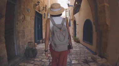 Sırt çantası ve kamerasıyla Jaffa 'daki eski bir şehir caddesinde yürüyen genç, narin bir turistin dikiz görüntüsü. Bir kadın...