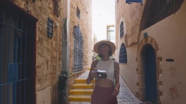 Sırt çantası ve kamerası olan genç bir kadın Jaffa 'daki eski bir şehir caddesinde yürüyor. Sırt çantalı bir kadın sokakta yürüyor.