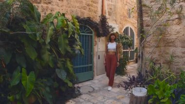 Sırt çantası ve kamerası olan genç bir kız eski bir şehir caddesinde yürüyor ve fotoğraf çekiyor. Sırt çantalı bir kadın yürür