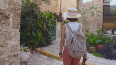 Sırt çantası ve kamerası olan genç bir kız eski bir şehir caddesinde yürüyor ve fotoğraf çekiyor. Sırt çantalı bir kadın yürür