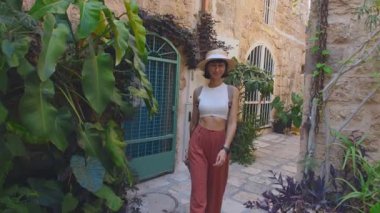 Sırt çantası ve kamerası olan genç bir kız eski bir şehir caddesinde yürüyor ve fotoğraf çekiyor. Sırt çantalı bir kadın yürür