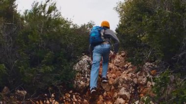 Sırt çantalı bir çocuk yolda yürüyor, ıslak taşlara basıyor. Arkadan bak. Gezinti ve yürüyüş.