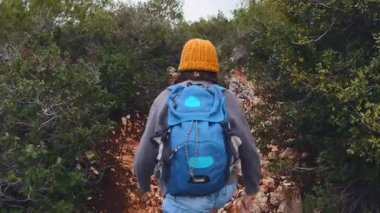 Sırt çantalı bir çocuk yolda yürüyor, ıslak taşlara basıyor. Arkadan bak. Gezinti ve yürüyüş.