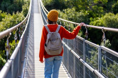 Sırt çantalı, şık giyinmiş yürüyüş yapan çekici, mutlu bir genç kız. Sırt çantalı bir kız köprüde yürüyor..