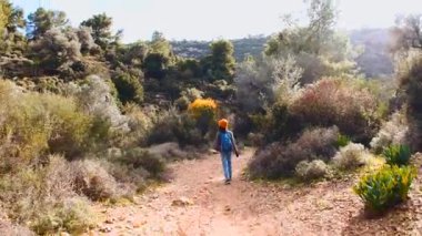 Maceralar ve seyahatler. Sırt çantalı bir çocuk dağ yolunda yürüyor. Çocuklarla seyahat..