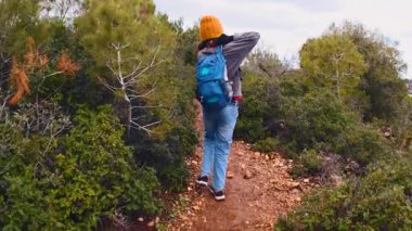 Bir çocuk yürür ve sırt çantasını takar. Maceralar ve seyahatler. Sırt çantalı bir çocuk dağ yolunda yürüyor. Arkadan bak. Seyahatler