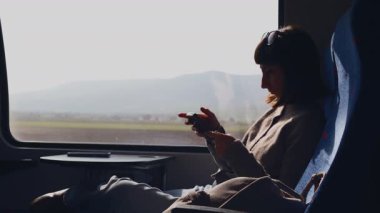 Trende cep telefonuyla mesajlaşan neşeli genç bir kadın. Trendeki bir kadının yan görüntüsü. Sosyal medyayı kullanan bir kız. Bir kız.