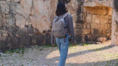 Sırt çantası ve fotoğraf makinesi olan genç bir kadın antik harabeleri keşfediyor. Kadın seyahat blogları ve belgeseller için video çekiyor.