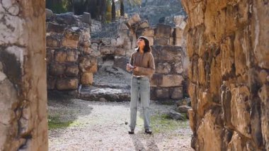 Blogu ve sosyal medyası için sırt çantalı şık bir turist. Antik taş kalıntıları yakınında bir turist