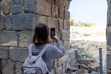 Sırt çantası ve fotoğraf makinesi olan genç bir kadın antik harabeleri keşfediyor. Kadın seyahat blogları, kültür ve turizm hakkında belgeseller için videolar çekiyor. blog için içerik oluşturur. Beit She 'an, İsrail.