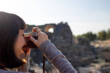 Kameralı bir kız. Blogu ve sosyal medyası için sırt çantalı bir turist. Bir turist fotoğrafları antik taş kalıntılarını gösteriyor..