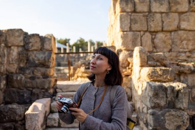 Sırt çantası ve fotoğraf makinesi olan genç bir kadın antik harabeleri keşfediyor. Kadın seyahat blogları, kültür ve turizm hakkında belgeseller için videolar çekiyor. blog için içerik oluşturur. Beit She 'an, İsrail.