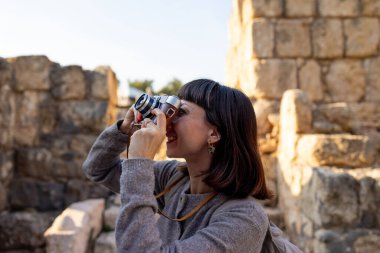 Sırt çantası ve fotoğraf makinesi olan genç bir kadın antik harabeleri keşfediyor. Kadın seyahat blogları, kültür ve turizm hakkında belgeseller için videolar çekiyor. blog için içerik oluşturur. Beit She 'an, İsrail.