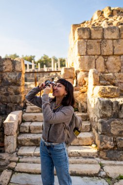 Blogu ve sosyal medyası için sırt çantalı şık bir turist. İsrail 'de antik taş kalıntıları yakınında bir turist. Beit She'an. Kameralı bir kız..