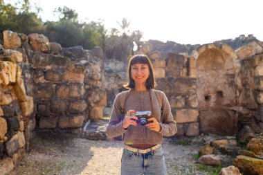Kameralı bir kız. Blogu ve sosyal medyası için sırt çantalı bir turist. Bir turist fotoğrafları antik taş kalıntılarını gösteriyor..