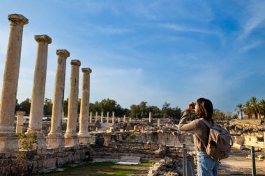 Blogu ve sosyal medyası için sırt çantalı şık bir turist. İsrail 'de antik taş kalıntıları yakınında bir turist. Beit She'an. Kameralı bir kız..