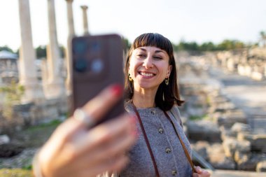Bir turist köşe yazılarına ve arkeolojik sitelere selfie çeker. Fotoğraf alçak bir açıdan çekilmiş. Sosyal medya için içerik oluşturur. İsrail 'i geziyorum, Beit She' an.