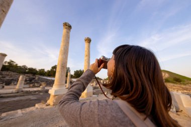 Blogu ve sosyal medyası için sırt çantalı şık bir turist. İsrail 'de antik taş kalıntıları yakınında bir turist. Beit She'an. Kameralı bir kız..