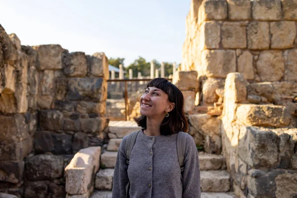 Sırt çantası ve fotoğraf makinesi olan genç bir kadın antik harabeleri keşfediyor. Kadın seyahat blogları, kültür ve turizm hakkında belgeseller için videolar çekiyor. blog için içerik oluşturur. Beit She 'an, İsrail.