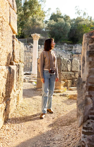 Sırt çantası ve fotoğraf makinesi olan genç bir kadın antik harabeleri keşfediyor. Kadın seyahat blogları, kültür ve turizm hakkında belgeseller için videolar çekiyor. blog için içerik oluşturur. Beit She 'an, İsrail.