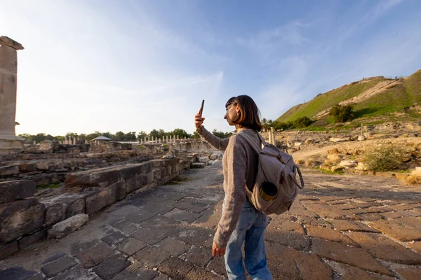 Bir kız içeriği çekiyor. Bir sırt çantasıyla harabeler arasında lüks bir turist gezintisi, blogu ve sosyal medyası için dönüm noktalarını fotoğraflamak. İsrail 'de antik taş kalıntıları yakınında bir turist. Beit She'an.