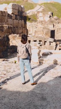 Dikey çekim. Bir sırt çantası ve kamerayla harabelerin arasında şık bir turist gezintisi. İsrail 'de antik taş kalıntıları yakınında bir turist