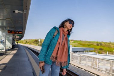 Platformda elinde telefonla tren bekleyen genç bir kadın var. Yolcunun biri telefonundaki uygulamayı kullanarak tren tarifesini kontrol ediyor. Karakolda bir kız var..