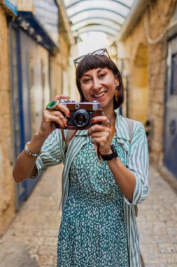 Kameralı çekici bir turist. Kameralı güzel bir kadın güzel yerlerin fotoğraflarını çeker. Kız kamerayı yüzüne doğru kaldırır ve fotoğraf çeker. Seyahat ve macera.