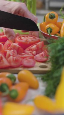 Sıcak bir mutfakta, bir adam domatesleri keser ve salata malzemelerini hazırlar. Sağlıklı beslenme. Mutfaktaki adam..